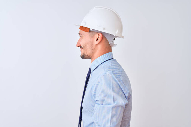 Молодий бізнесмен в підрядному шоломі безпеки над ізольованим тлом, дивлячись в бік, розслабляє профільну позу з природним обличчям з впевненою посмішкою
. - Фото, зображення