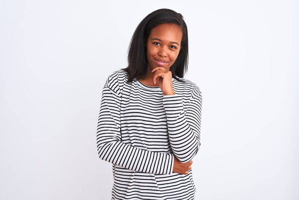 Bella giovane donna afroamericana che indossa maglione invernale su sfondo isolato guardando fiducioso la fotocamera sorridente con le braccia incrociate e la mano sollevata sul mento. Pensare positivo
. - Foto, immagini