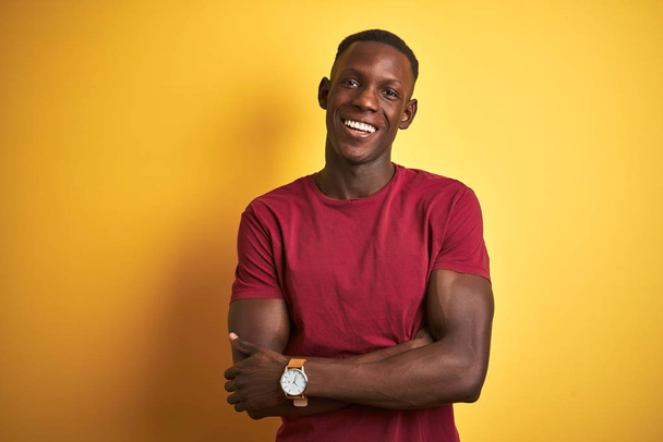 Молодой африканский американец в красной футболке стоит на изолированном желтом фоне счастливое лицо улыбается со скрещенными руками, глядя в камеру. Позитивный человек
. - Фото, изображение