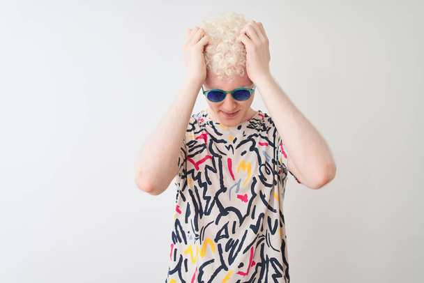 Young albino blond man wearing colorful t-shirt and sunglasses over isolated red background suffering from headache desperate and stressed because pain and migraine. Hands on head. - Photo, image
