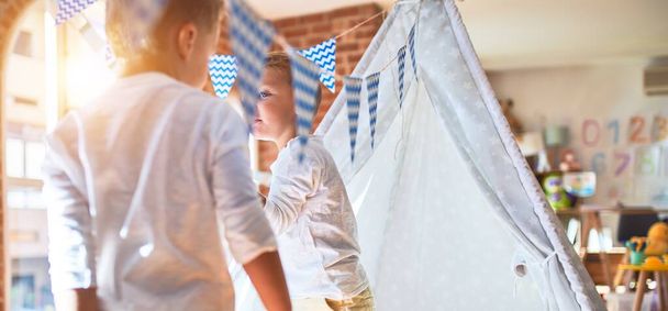 Adorable blonde twins playing inside tipi around lots of toys at kindergarten - 写真・画像
