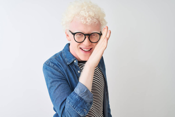 Young albino blond man wearing denim shirt and glasses over isolated white background hand on mouth telling secret rumor, whispering malicious talk conversation - Fotoğraf, Görsel