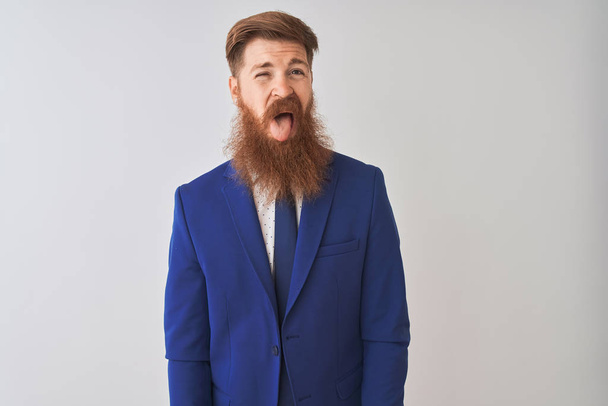 Young redhead irish businessman wearing suit standing over isolated white background sticking tongue out happy with funny expression. Emotion concept. - Photo, Image