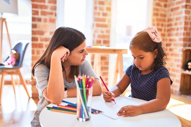 Belle enseignante et tout-petit dessin de fille à l'aide de crayons de couleur à la maternelle
 - Photo, image