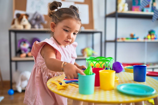 Młody piękny maluch bawiący się sztućcami i zabawkami spożywczymi na stole w przedszkolu - Zdjęcie, obraz