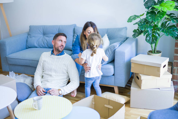 Beautiful family, parents sitting on the sofa drinking coffee looking his kid playing at new home around cardboard boxes - Фото, зображення