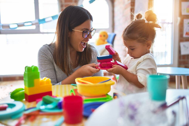 Joven hermosa maestra y niño pequeño jugando con comida plástica y juguetes de cuchillería en el jardín de infantes
 - Foto, imagen