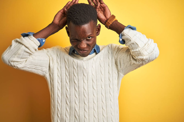 Uomo afroamericano che indossa camicia di jeans e maglione bianco su sfondo giallo isolato Fare coniglietto orecchie gesto con le mani palme cercando cinico e scettico. Concetto di coniglio pasquale
. - Foto, immagini