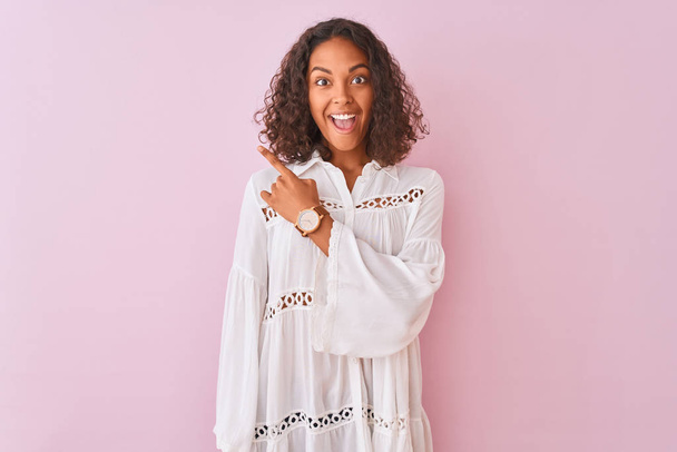 Young brazilian woman wearing shirt standing over isolated pink background cheerful with a smile of face pointing with hand and finger up to the side with happy and natural expression on face - Photo, Image