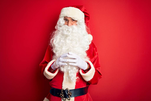 Ein gutaussehender Mann mittleren Alters im Weihnachtsmannkostüm steht über vereinzelten roten Hintergrundhänden zusammen und drückt lächelnd entspannt und fröhlich die Daumen. Erfolg und Optimismus - Foto, Bild