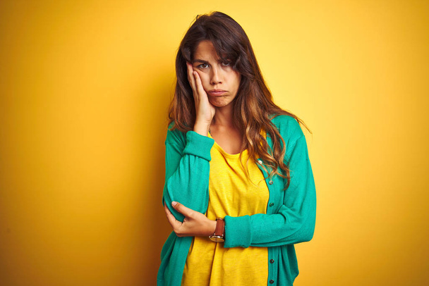 Fiatal nő visel póló és zöld pulóver áll felett ordítozó elszigetelt háttér gondolkodás fáradtnak tűnik, és unatkozik a depresszió problémák keresztbe karok. - Fotó, kép
