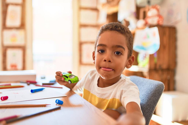 Hermoso niño afroamericano sentado en el escritorio jugando con coches en el jardín de infantes
 - Foto, imagen