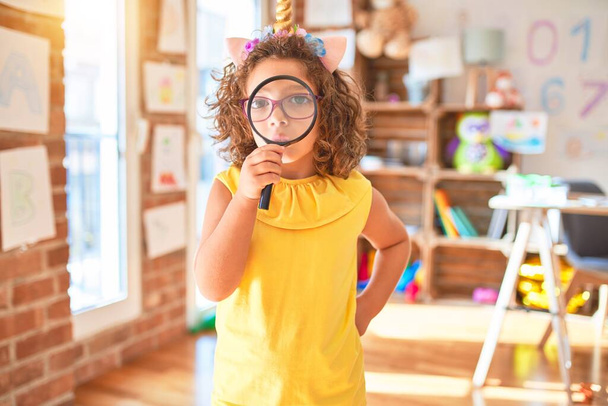 Beau bambin debout portant des lunettes et licorne diadème en utilisant loupe à la maternelle
 - Photo, image