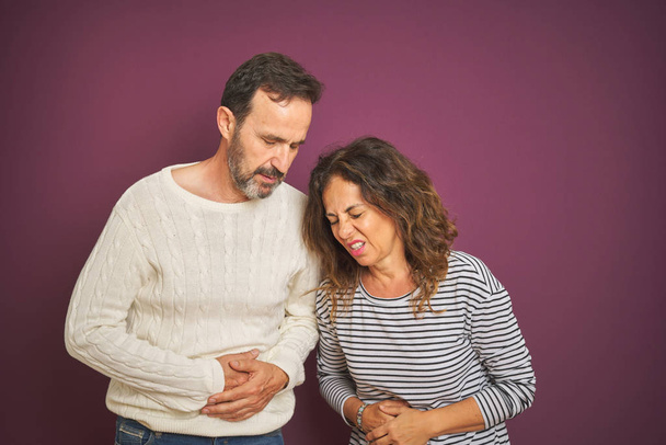 Beau couple d'âge moyen portant un pull d'hiver sur fond violet isolé avec la main sur le ventre parce que l'indigestion, la maladie douloureuse se sentent mal. Concept Ache
. - Photo, image