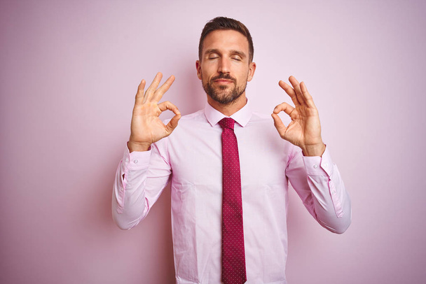 Business man wearing tie and elegant shirt over pink isolated background relax and smiling with eyes closed doing meditation gesture with fingers. Yoga concept. - Foto, Imagem