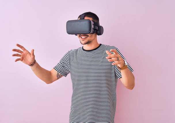 Νεαρός παίζει βιντεοπαιχνίδι φορώντας γυαλιά εικονικής πραγματικότητας, κοιτάζοντας εικονική προσομοίωση κατάπληκτος και χαμογελαστός χαρούμενος - Φωτογραφία, εικόνα