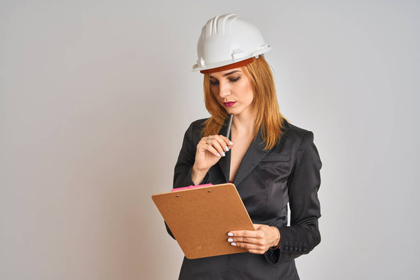 Young beautiful redhead architect woman wearing suit and hardhelmet holding flip board - Fotografie, Obrázek