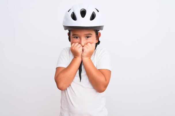 Piękny chłopiec noszący kask ochrony roweru stojący nad odizolowanym białym tłem wyglądający na zestresowanego i nerwowego z rękami obgryzającymi paznokcie. Problem lękowy. - Zdjęcie, obraz