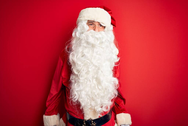 Homem bonito de meia idade vestindo traje de Papai Noel em pé sobre fundo vermelho isolado irritado e louco gritando frustrado e furioso, gritando com raiva. Raiva e conceito agressivo
. - Foto, Imagem