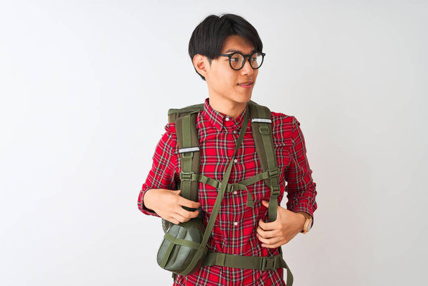 Chinese hiker man wearing backpack canteen glasses over isolated white background looking away to side with smile on face, natural expression. Laughing confident. - Valokuva, kuva