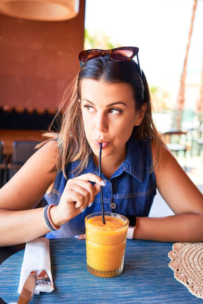 Nuori kaunis nainen istuu ravintolassa nauttien kesälomasta juoden terveellistä smoothie
 - Valokuva, kuva
