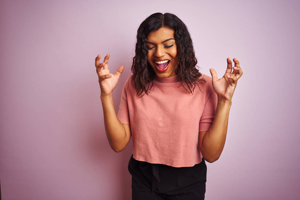 Young beautiful transsexual transgender elegant woman over isolated pink background celebrating mad and crazy for success with arms raised and closed eyes screaming excited. Winner concept - Foto, Imagen