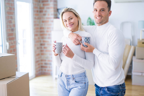Jovem casal bonito de pé beber xícara de café em casa nova em torno de caixas de papelão
 - Foto, Imagem