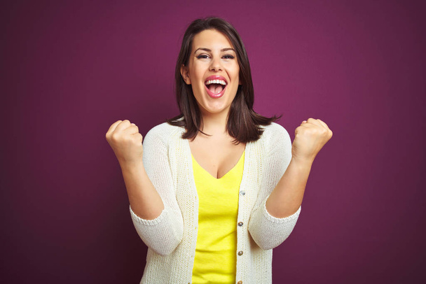 Young beautiful brunette woman a jacket over purple isolated background celebrating surprised and amazed for success with arms raised and open eyes. Winner concept. - Foto, Bild