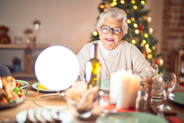 Schattige oudere vrouw die blij en zelfverzekerd lacht. Zittend bereid om thuis kerst te vieren - Foto, afbeelding