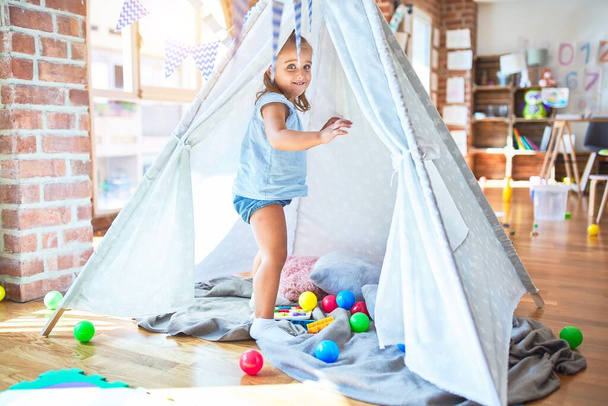 Young beautiful blonde girl kid enjoying play school with toys at kindergarten, smiling happy playing inside indian tent at home - Photo, Image