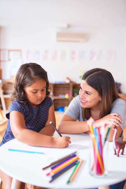 Beautiful teacher and toddler girl drawing draw using colored pencils at kindergarten - Zdjęcie, obraz