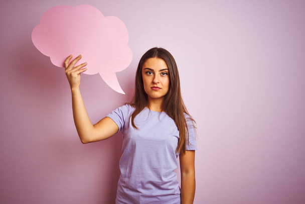 Young beautiful woman holding cloud speech bubble over isolated pink background with a confident expression on smart face thinking serious - Photo, Image