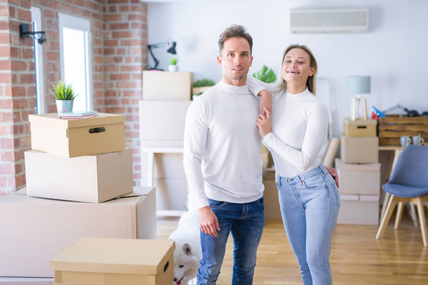 Young beautiful couple standing at new home around cardboard boxes - Photo, Image