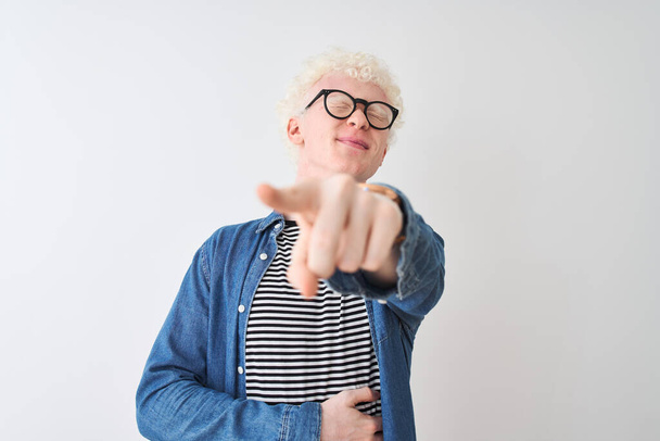 Jeune homme blond albinos portant chemise en denim et lunettes sur fond blanc isolé se moquant de vous, pointant du doigt la caméra avec la main sur le corps, expression de honte
 - Photo, image