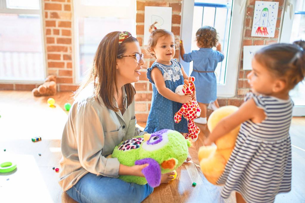 Kaunis opettaja ja ryhmä pikkulapsia leikkimässä paljon leluja päiväkodissa
 - Valokuva, kuva