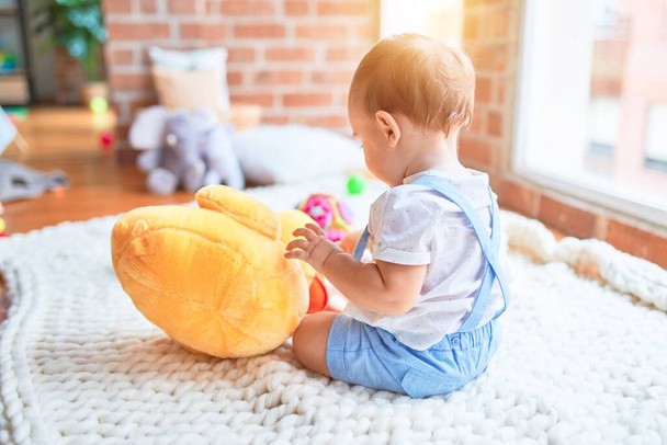 Gyönyörű kisbaba ül a takarón, kacsa babával játszik az óvodában. - Fotó, kép