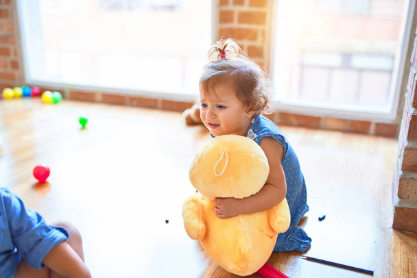Adorable toddler sitting on the floor playing with duck doll around lots of toys at kindergarten - Photo, Image