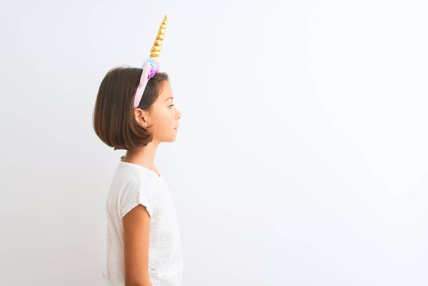 Beautiful child girl wearing unicorn diadem standing over isolated white background looking to side, relax profile pose with natural face with confident smile. - Photo, image