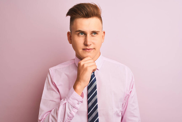 Young handsome businessman wearing shirt and tie standing over isolated pink background with hand on chin thinking about question, pensive expression. Smiling and thoughtful face. Doubt concept. - Фото, изображение