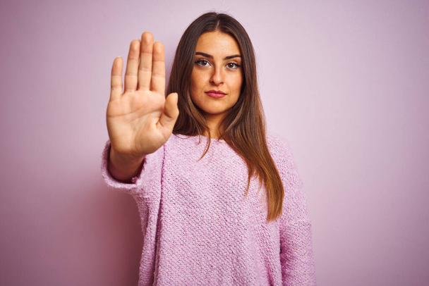Young beautiful woman wearing casual sweater standing over isolated pink background doing stop sing with palm of the hand. Warning expression with negative and serious gesture on the face. - Foto, Bild