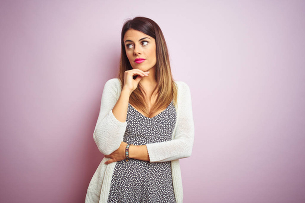 Young beautiful woman standing over pink isolated background with hand on chin thinking about question, pensive expression. Smiling with thoughtful face. Doubt concept. - Photo, Image