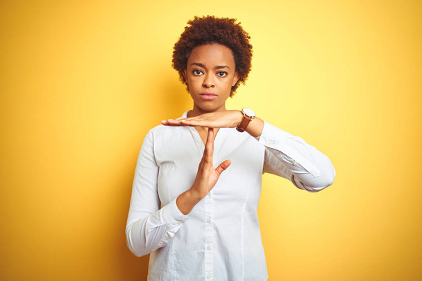 Afrykański amerykański biznes kobieta na odizolowanym żółtym tle robi czas na gest z rąk, sfrustrowany i poważny twarz - Zdjęcie, obraz