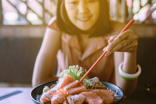 Hands asian woman using chopsticks with raw salmon fillet on dish in restaurant - Фото, изображение