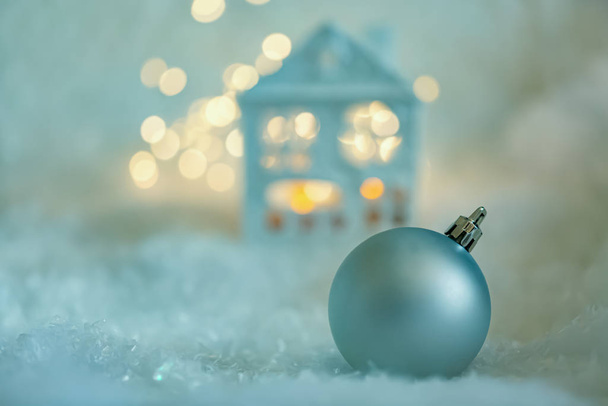 Tebrik kartı. Mutlu Noeller. Mavi ev karla kaplı, bir top, bir çelenk ve yeşil dallarla. Yumuşak odak - Fotoğraf, Görsel