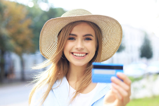 Cheerful young optimistic girl standing outdoors, holding credit card in hand. - Foto, Imagem