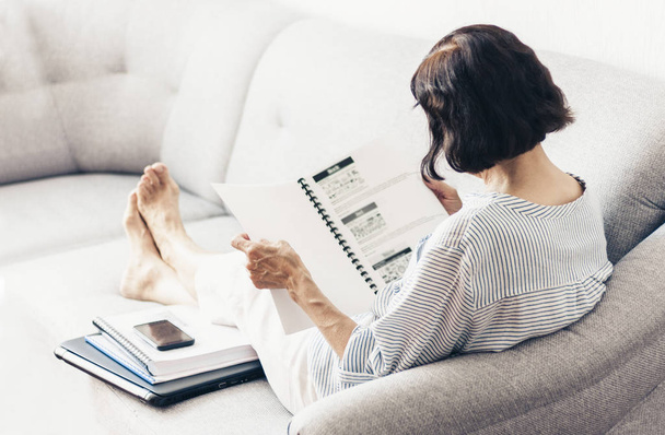 Middle-aged brunette woman on the gray sofa reading documents, u - Zdjęcie, obraz