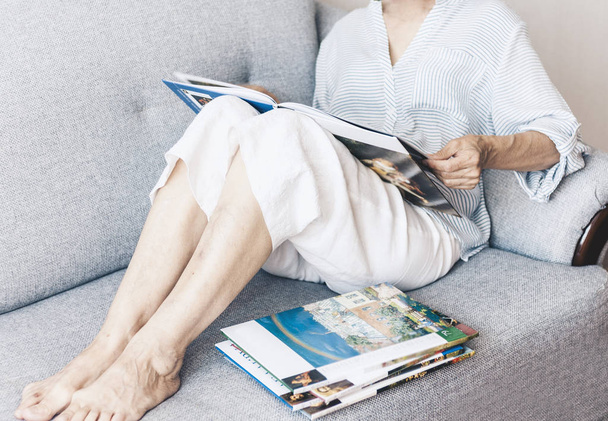 Donna bruna di mezza età sul divano grigio guardando l'album con spirito
 - Foto, immagini