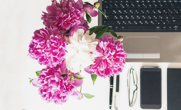 bouquet of pink peonies, laptop, smartphone, pens, glasses and a - Фото, изображение
