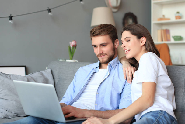 Young couple doing some online shopping at home, using a laptop on the sofa. - Фото, изображение