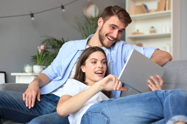 Young couple watching media content online in a tablet sitting on a sofa in the living room. - Fotoğraf, Görsel